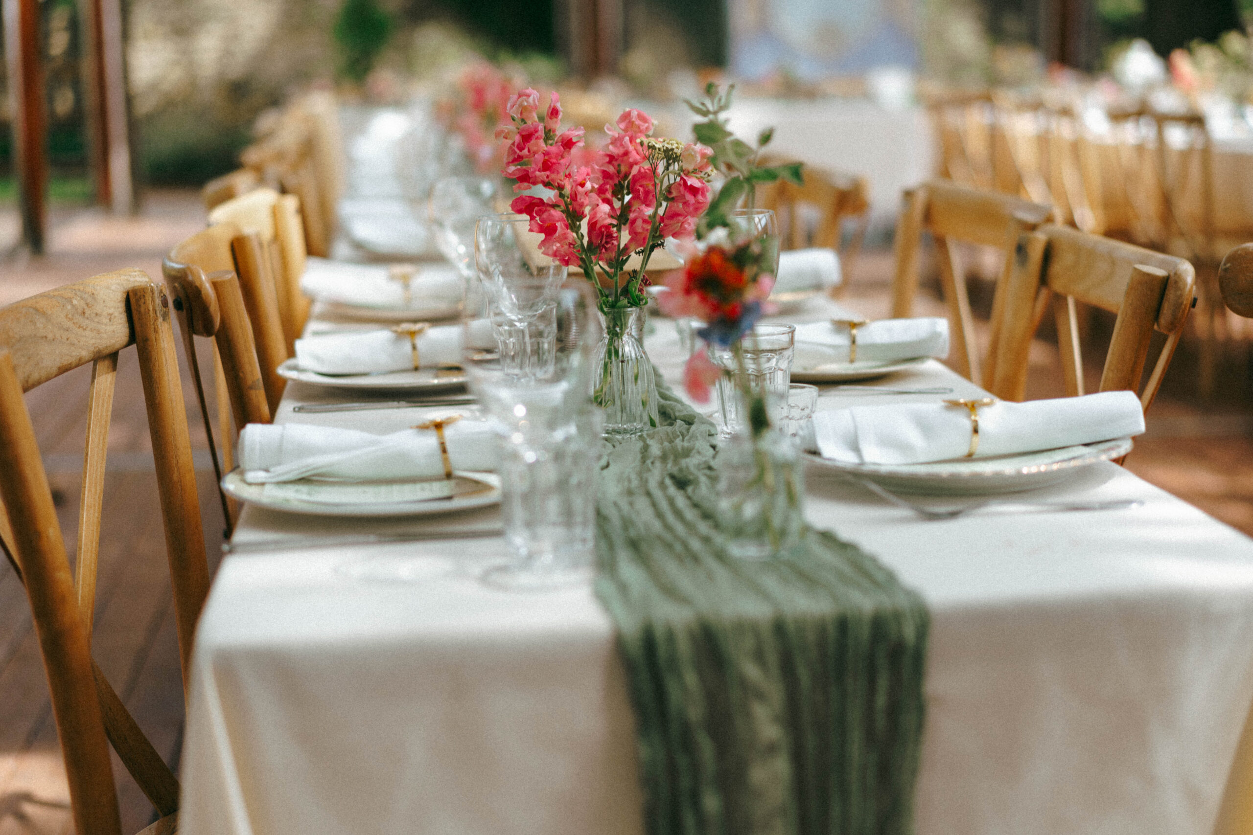 Reception table setting with a green linen runner, wildflower posies in glass bud vases, and place settings at Caitlin & Joe's Meadley Walled Garden wedding