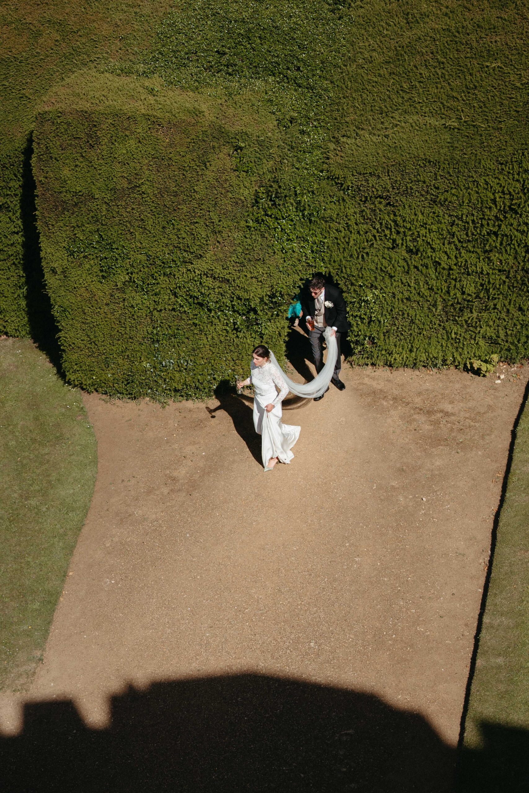 Aerial photograph of a bride and groom walking beside the clipped yew hedges at Rousham House