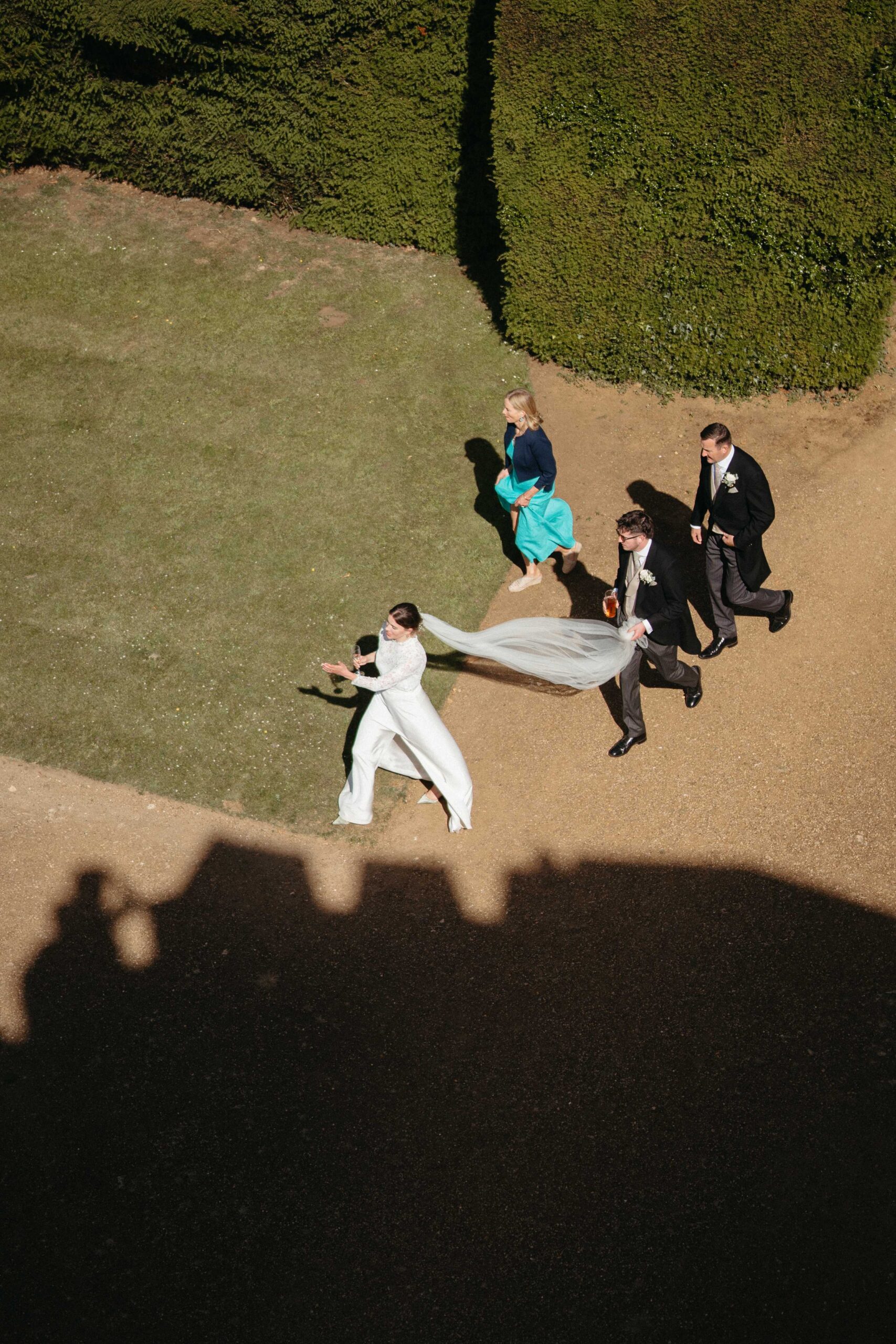 Aerial view of the bride and groom walking through the gardens with guests at Rousham House