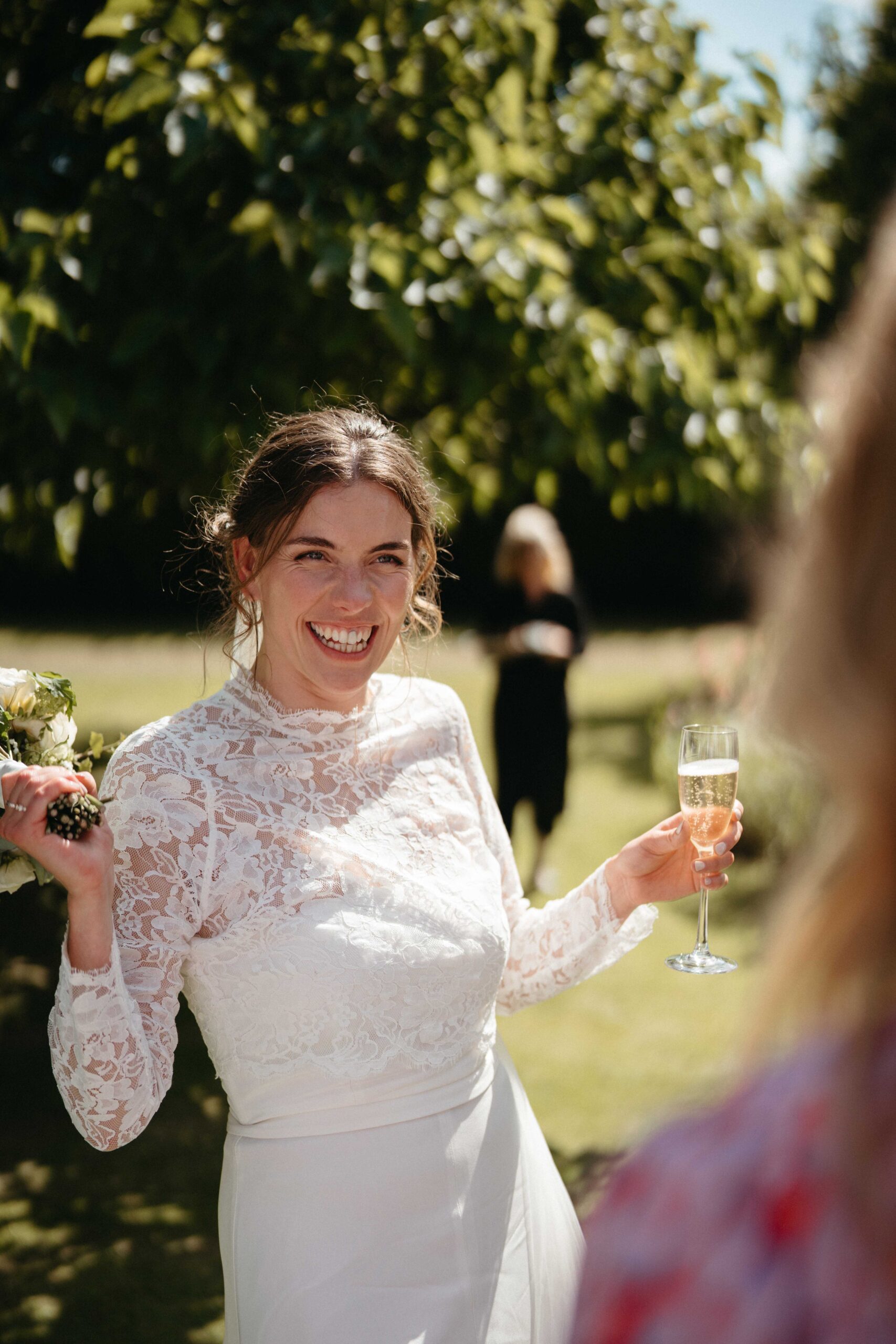 Bride laughing with a glass of champagne in the gardens at Rousham House