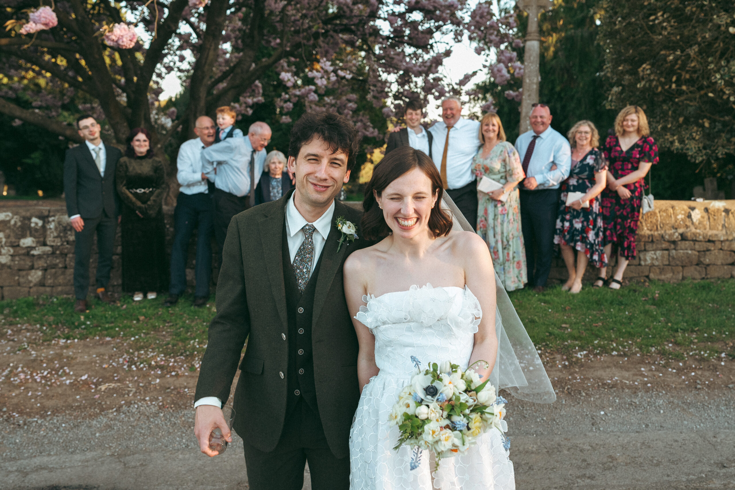 Bride and groom laughing together with wedding guests in the background, a candid documentary-style moment