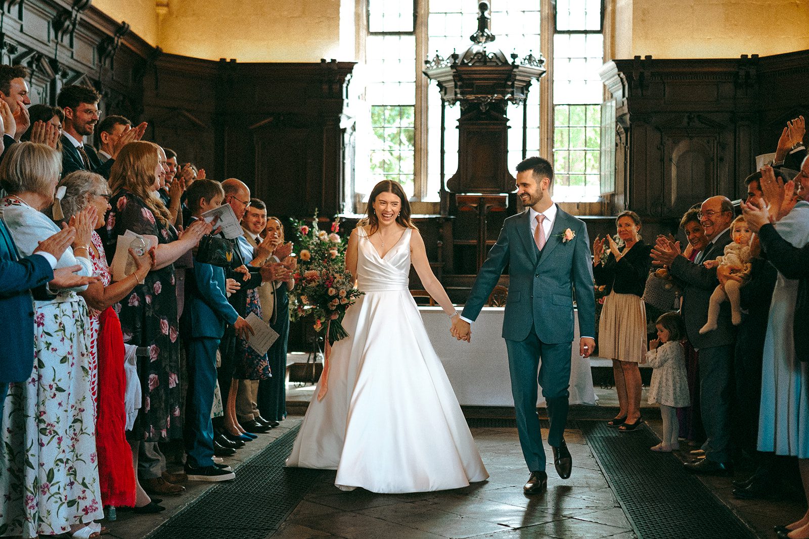 Bride and groom walking back down the aisle through confetti in the Divinity School at the Bodleian Libraries, Oxford