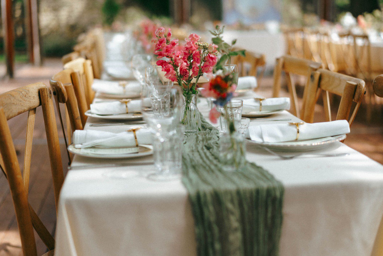 Reception table setting with a green linen runner, wildflower posies in glass bud vases, and place settings at Caitlin & Joe's Meadley Walled Garden wedding