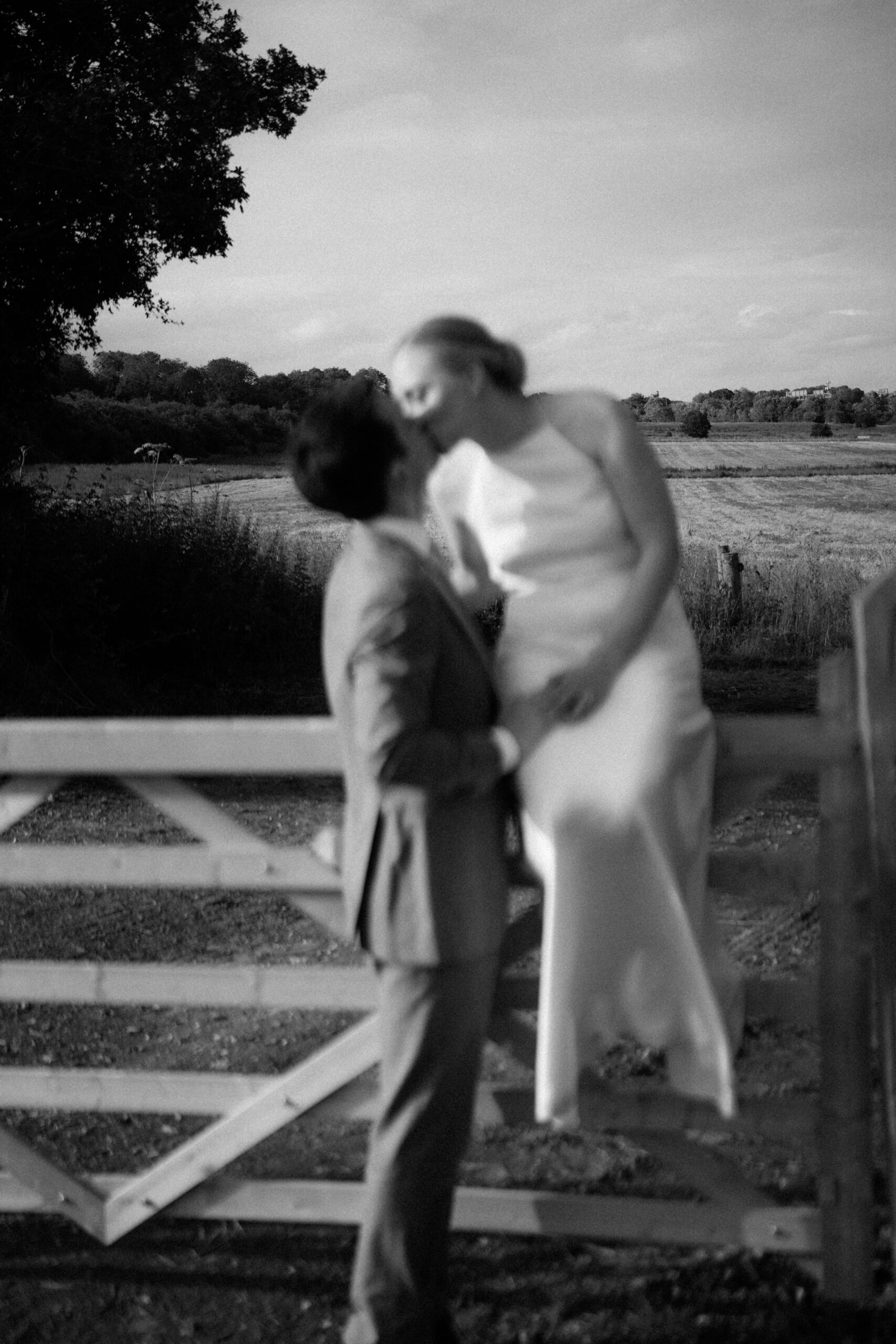 Black and white photograph of a couple by a field gate, documentary wedding photography