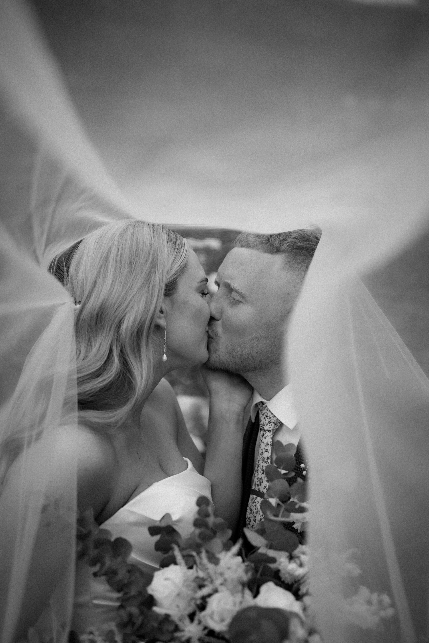 Black and white close-up of a bride and groom kissing under a veil